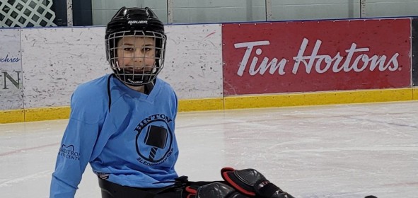 Sledge hockey player sitting in sled in blue jersey smiling