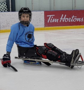 Sledge hockey player sitting in sled in blue jersey smiling